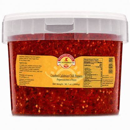 A clear plastic tub filled with crushed red chili peppers, featuring a yellow label with the Instituto Latino brand logo and product details, set against a plain white background.