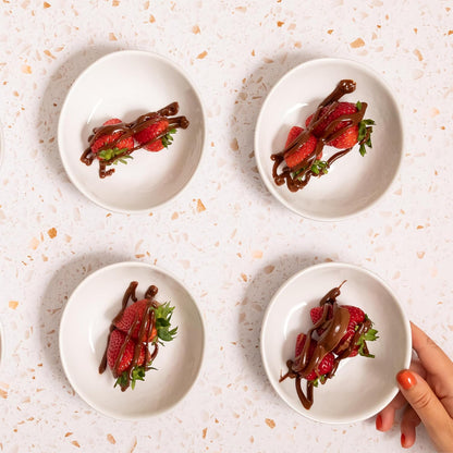 Four white plates with strawberries and chocolate sauce on a light speckled surface.