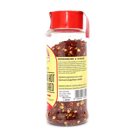 Shaker of red pepper flakes with a red lid on a white background