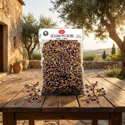 Bag of Sicilian pistachios on a wooden table with an olive tree and stone building in the background.