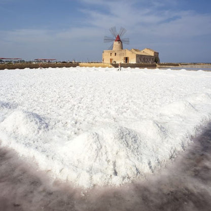 Salt piles with a windmill in the background under a blue sky.