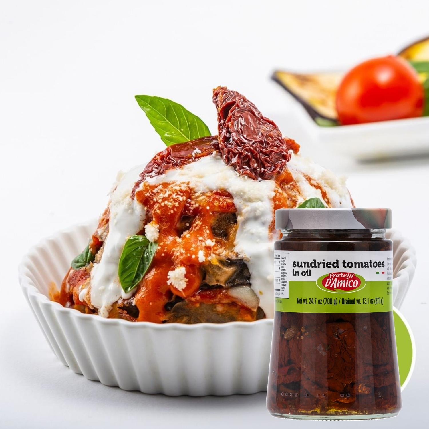 Fratelli D’Amico Sun-Dried Tomatoes in Oil, 24.7 oz (700 g) jar displayed in front of a gourmet dish of baked eggplant parmigiana topped with tomato sauce, ricotta, basil leaves, and a sun-dried tomato garnish